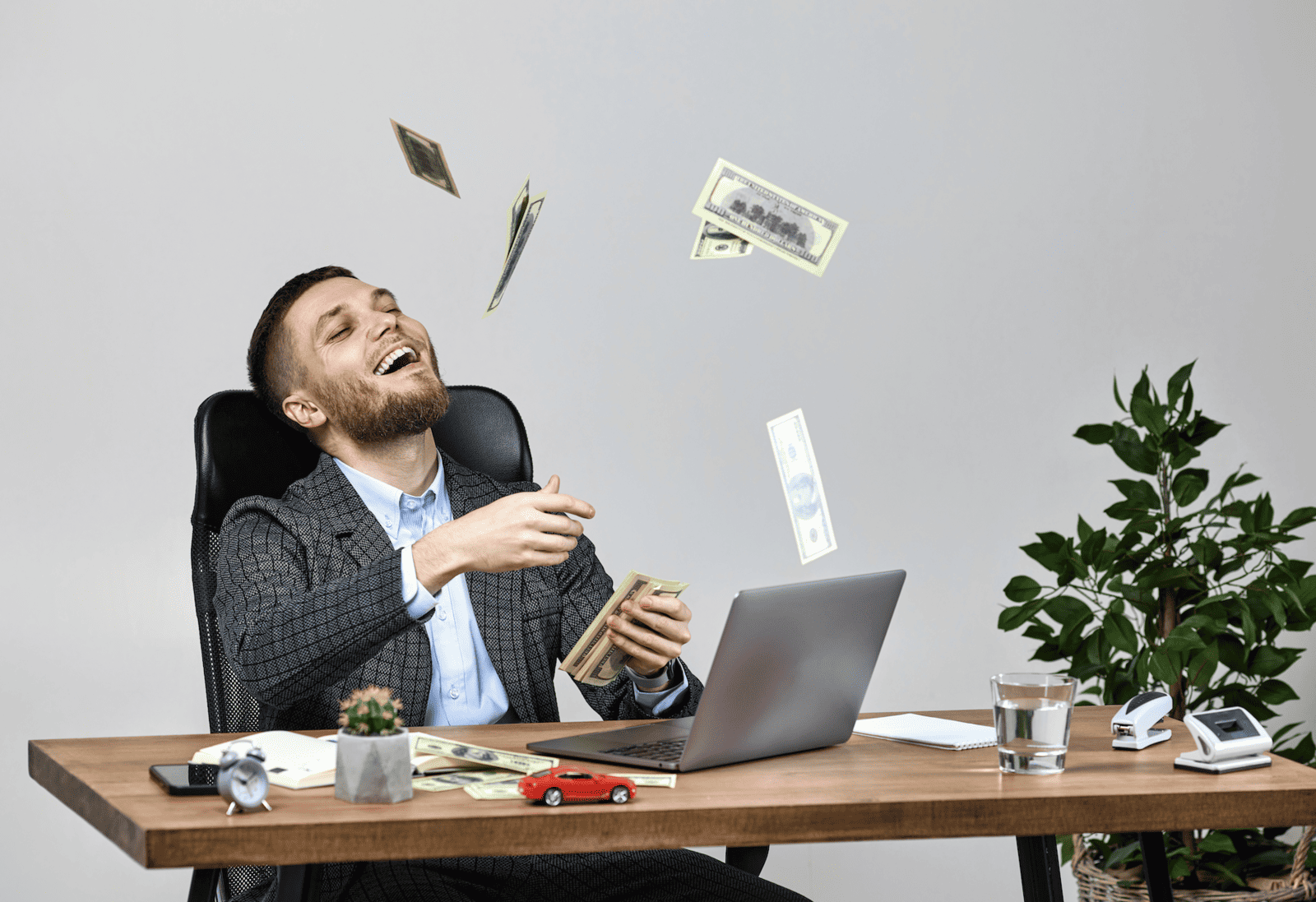 Young businessman at desk throwing money in the air